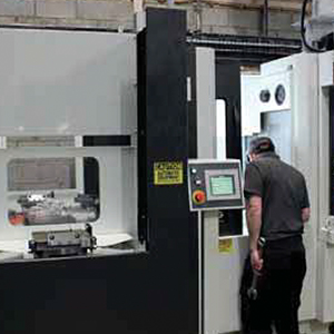 An engineer operates a Kitamura horizontal machining center inside a workshop, with visible control panel and metal component set up inside the machine.