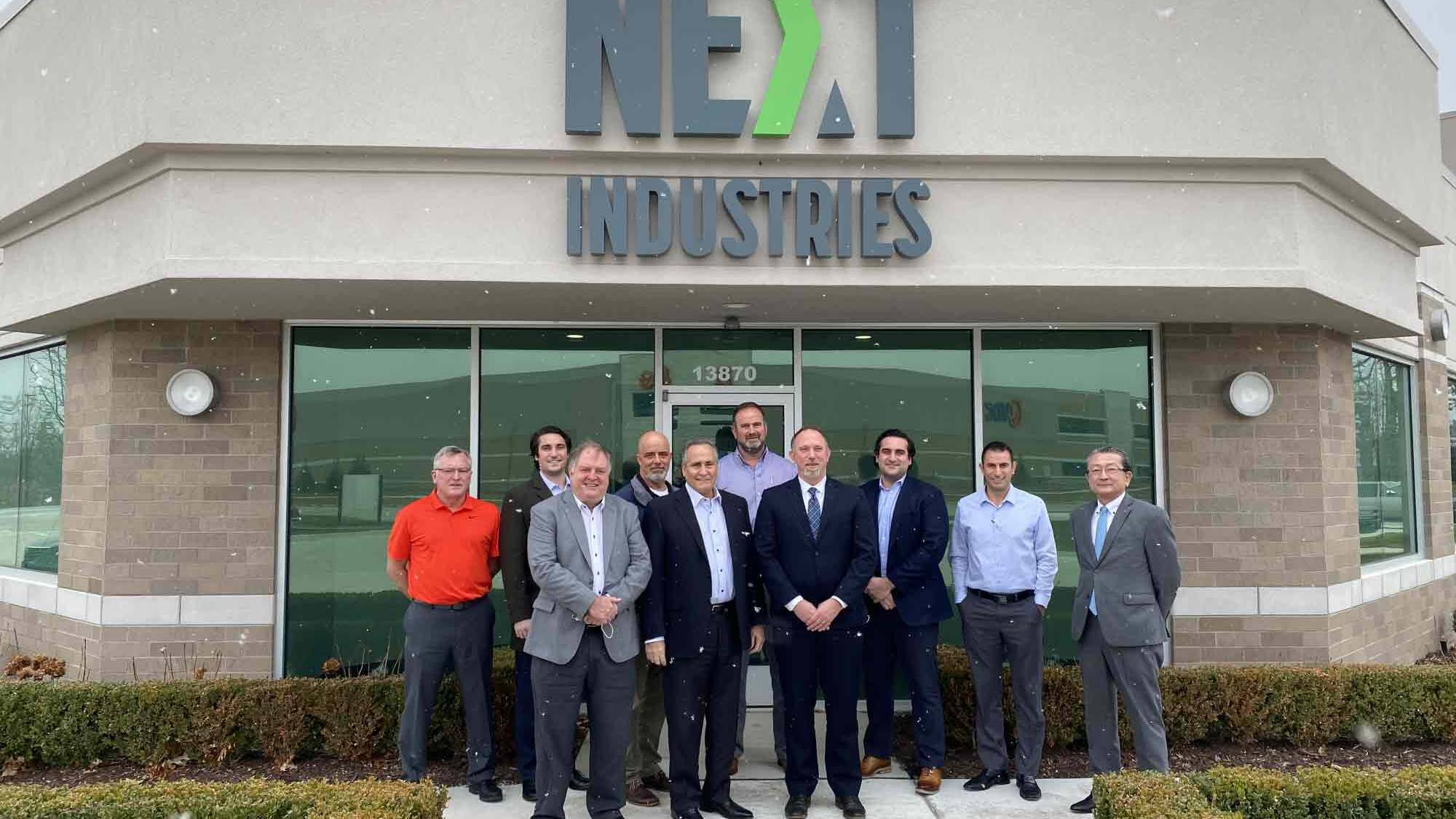 A group of business men smiling and standing outside a Next Industries shop.