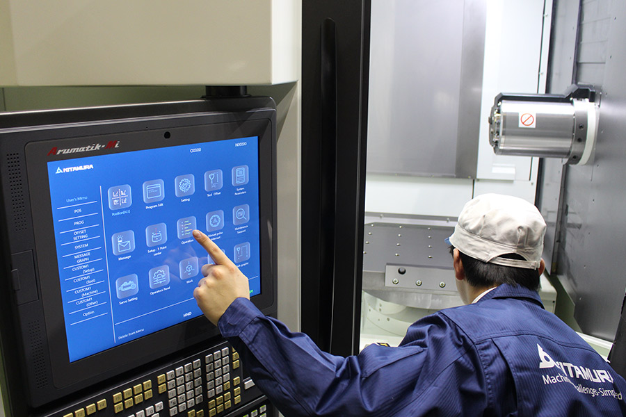 Operator uses touch screen control panel on a Kitamura CNC machine, preparing the horizontal machining center for operation.