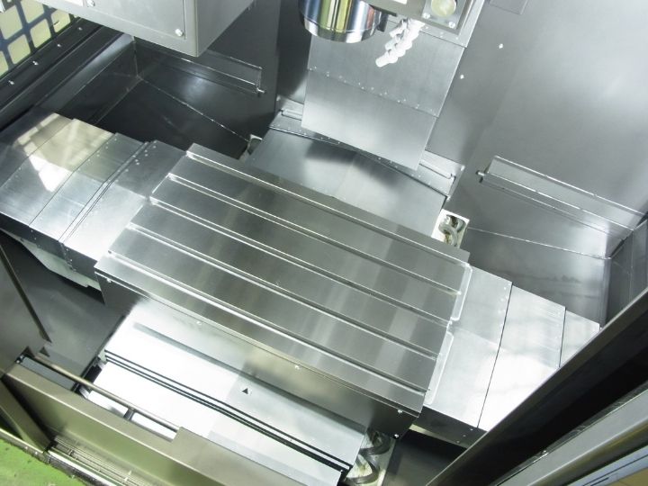 CNC machine workspace with a large metal worktable and vertical spindle.