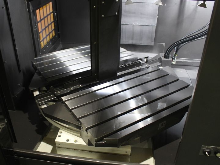 CNC machine workspace with a tilting metal worktable and precision guide rails.