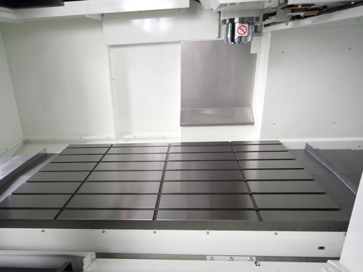 CNC machine workspace with a large metal worktable and vertical spindle.