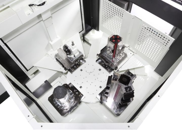 CNC machine interior with a rotary table and multiple workpiece fixtures.