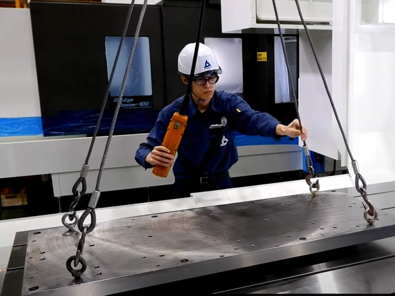 A machine operator hooking up a block of metal with cables.