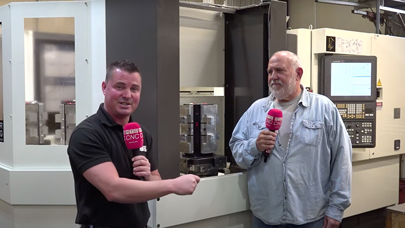 Two people in front of industrial machine talking on an interview.