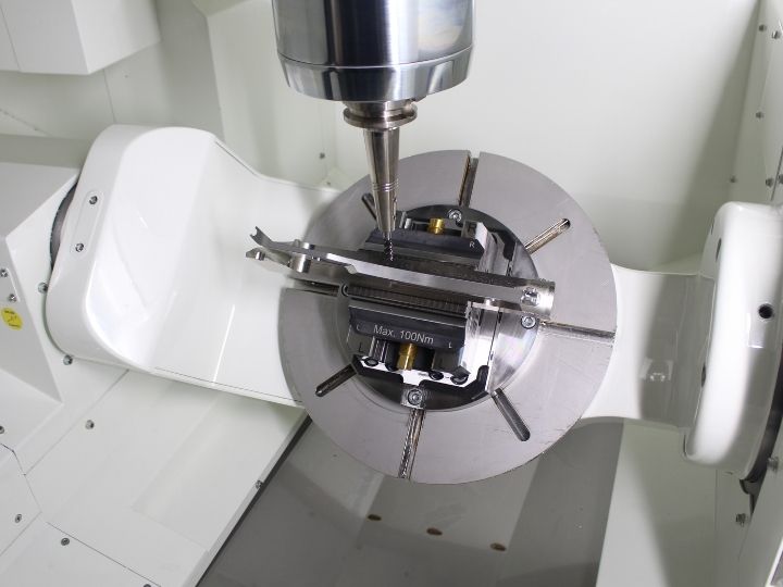 Close-up of a Kitamura Mytrunnion-4G CNC machine performing precision machining on a component secured in a rotary table fixture.