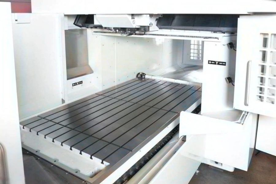 Interior view of a bridge-style machining center showcasing a large T-slot worktable and overhead gantry system for heavy-duty milling operations.