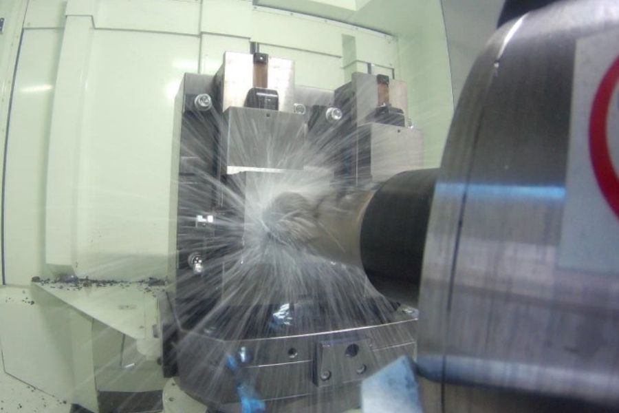 Close-up of a horizontal machining center (HMC) in action, with coolant spraying as the cutting tool machines a metal workpiece in a vise.