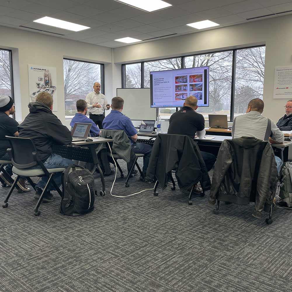Instructor presents to a group of professionals in a Kitamura training room, with laptops open and presentation on screen.