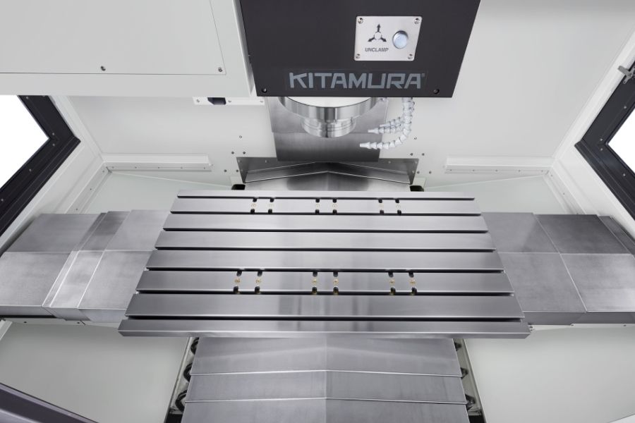 Top-down view inside a Kitamura vertical machining center, highlighting the precision-ground T-slot worktable and spindle head with coolant nozzles.