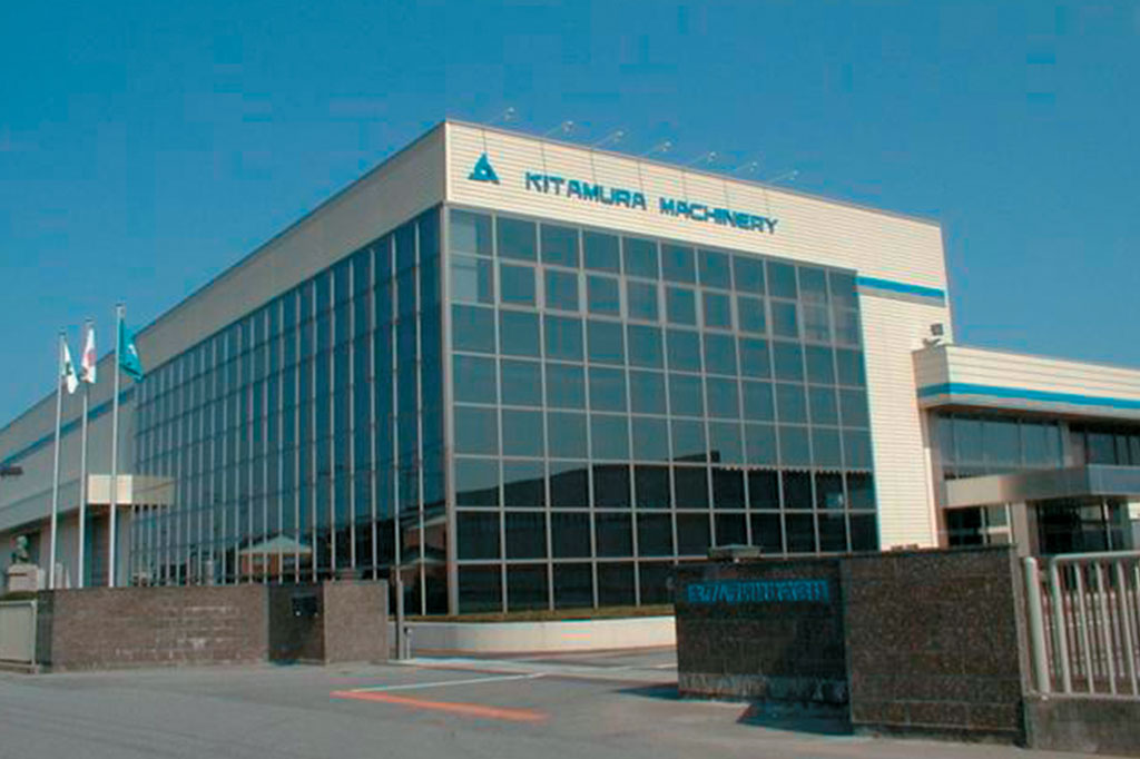 Exterior view of the Kitamura Machinery building with glass-paneled facade, blue sky, and company signage prominently displayed.