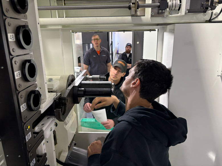 **Alt text:** Technician operating a machine while others observe and take notes during a hands-on training session in a manufacturing facility.